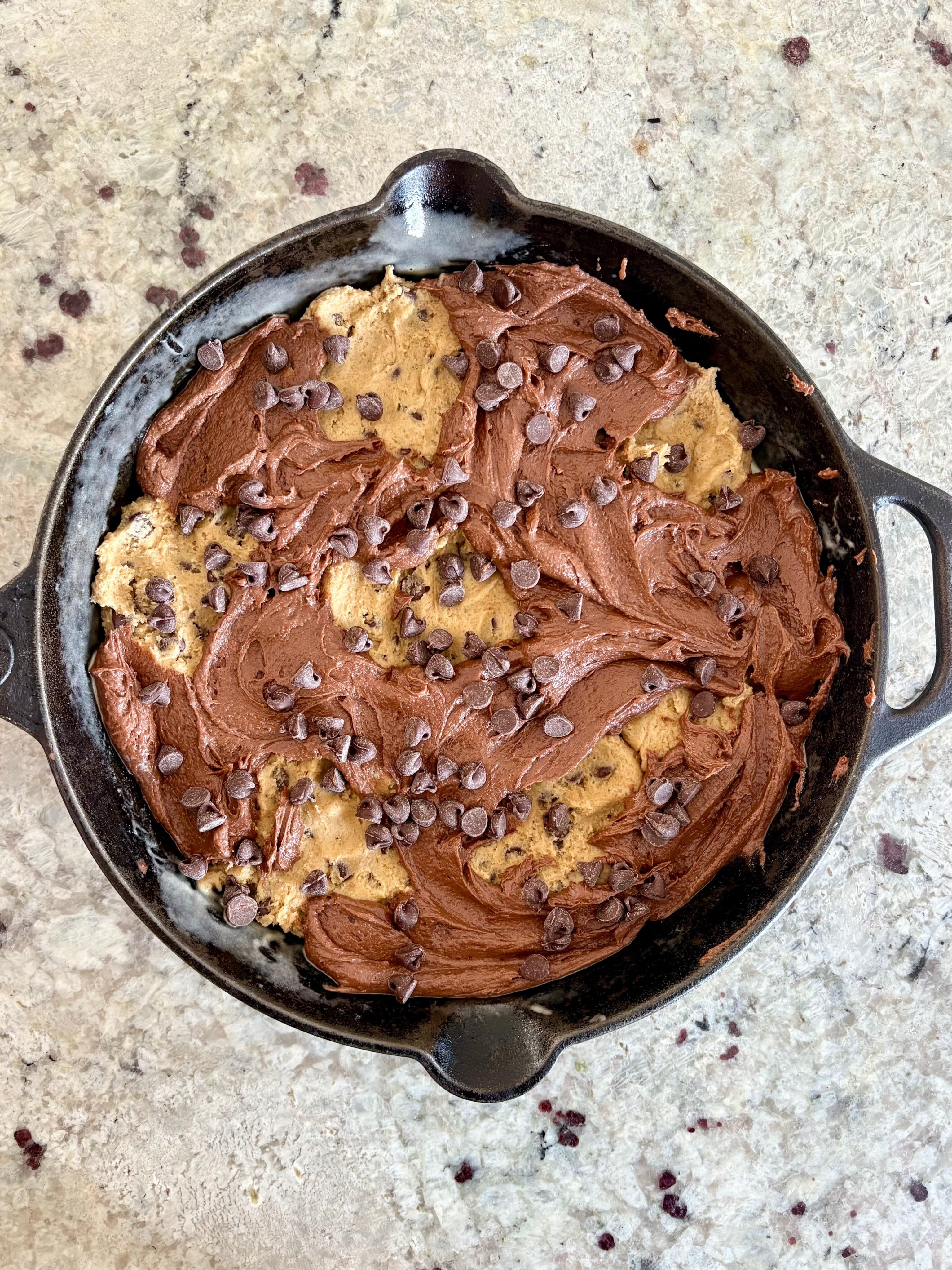 Overhead shot of an unbaked skillet Brownie and chocolate chip cookie, topped with chocolate chips.